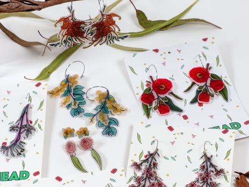 Queensland native flower earrings laid flat amongst gum leaves.